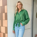 Woman wearing a green shirt and blue jeans standing against a tiled wall.